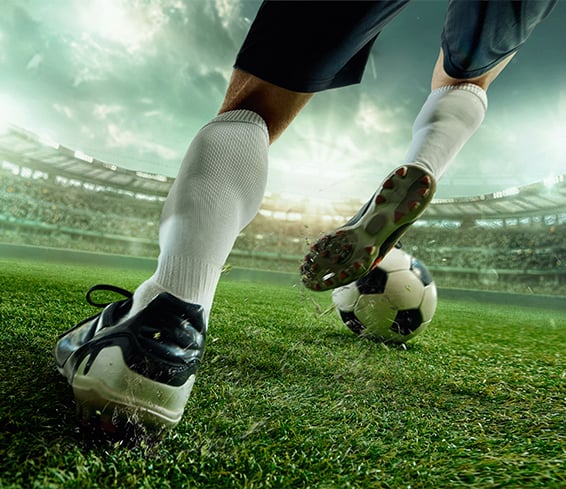 Soccer player in white socks kicking the football on green stadium field.